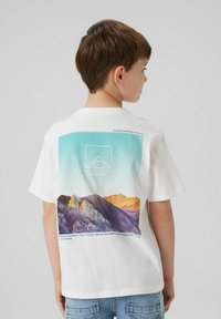 T-shirt en coton blanc avec un graphique de montagne aux tons bleus et violets au dos. Comprend du texte et un design de logo géométrique.