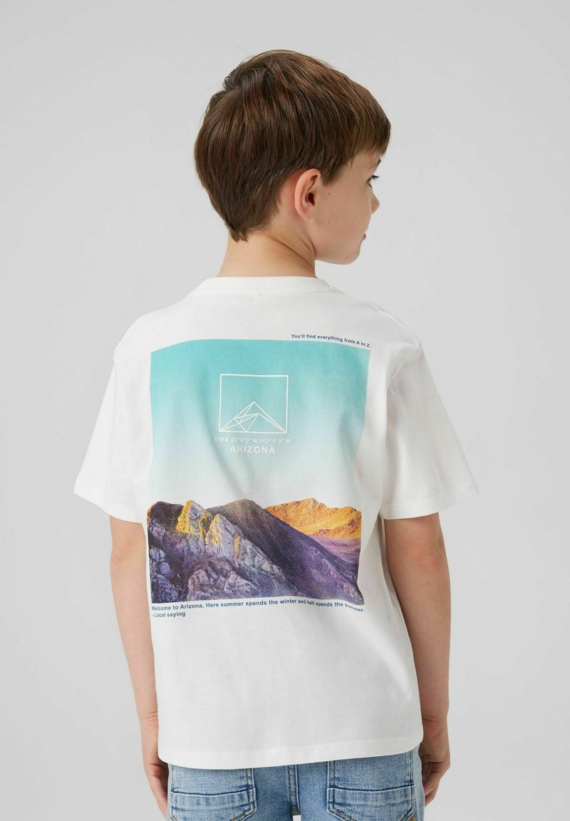 T-shirt en coton blanc avec un graphique de montagne aux tons bleus et violets au dos. Comprend du texte et un design de logo géométrique.