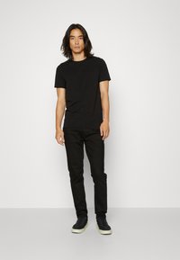 T-shirt noir à manches courtes, associé à un jean skinny noir et des baskets noires avec une semelle claire. Design simple et ajusté.