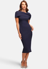 Dunkelblaues Schulterfreies Kleid mit figurbetontem Schnitt, knie-langer Saum und strukturiertem Stoff. Kombiniert mit silbernen High-Heels.