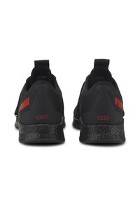 Zapatillas deportivas negras con parte superior de malla, con marca roja contrastante en el talón y suela negra texturizada. Diseño tipo slip-on con lengüeta.