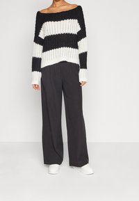 Pull en maille à rayures noires et blanches avec un design épaules dénudées et une texture côtelée. Associé à un pantalon noir ample et des baskets blanches.