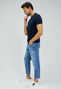 Camiseta de cuello redondo azul marino, jeans ajustados de mezclilla claros y zapatillas blancas con detalles en azul marino. Un conjunto simple y casual con un corte moderno.