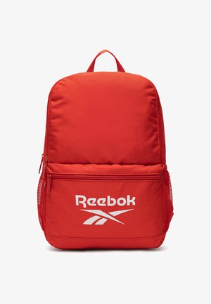 Mochila roja de Reebok con bolsillo frontal con cremallera, bolsillos laterales de malla y asa superior para llevar. Logo blanco de Reebok impreso en el bolsillo frontal.