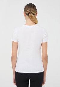 Biała bawełniana koszulka z krótkim rękawem, okrągłym dekoltem i dopasowanym krojem, widziana z tyłu. Gładka tekstura, brak widocznych wzorów.