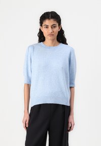 Suéter tricotado azul claro com mangas curtas bufantes, gola e bainha caneladas, corte solto, usado sobre calças pretas. Textura suave.