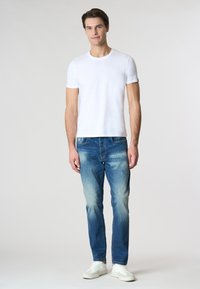 T-shirt bianco a girocollo con logo sottile, abbinato a jeans in denim blu sbiadito e sneakers bianche. Look casual con un fit classico.
