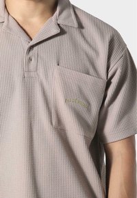 Koszulka polo z krótkim rękawem, z kołnierzykiem w jasnoróżowej strukturze waflowej, z kieszenią na piersi i subtelnym haftem zielonego logo.