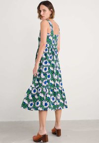 Rochie midi florală cu o paletă de culori albastră și verde, cu margarete albe, spate elasticizat și fustă stratificată. Purtați cu tocuri maro.