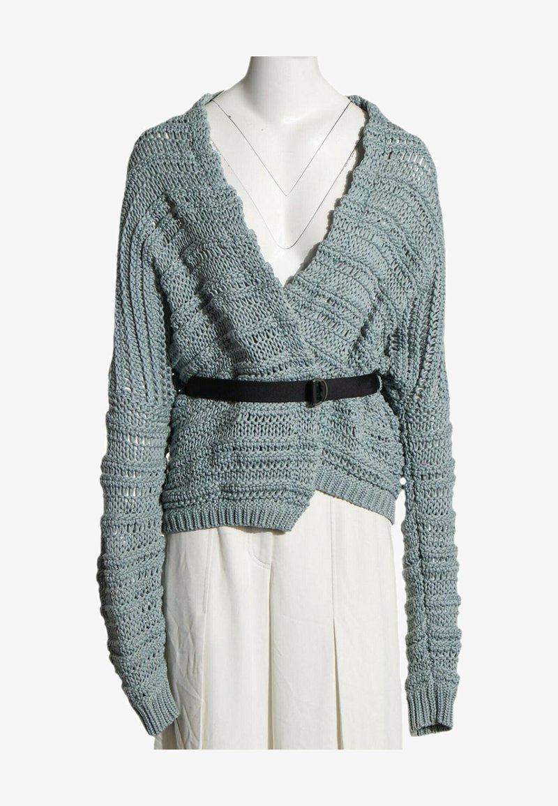 Pull court en maille épaisse bleu clair avec manches longues et col en V profond, associé à une ceinture noire et un bas blanc.