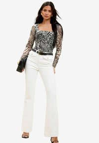 Long-sleeve top with a fitted square neckline in a black and beige animal print, paired with high-waisted white flared jeans and a black bag.