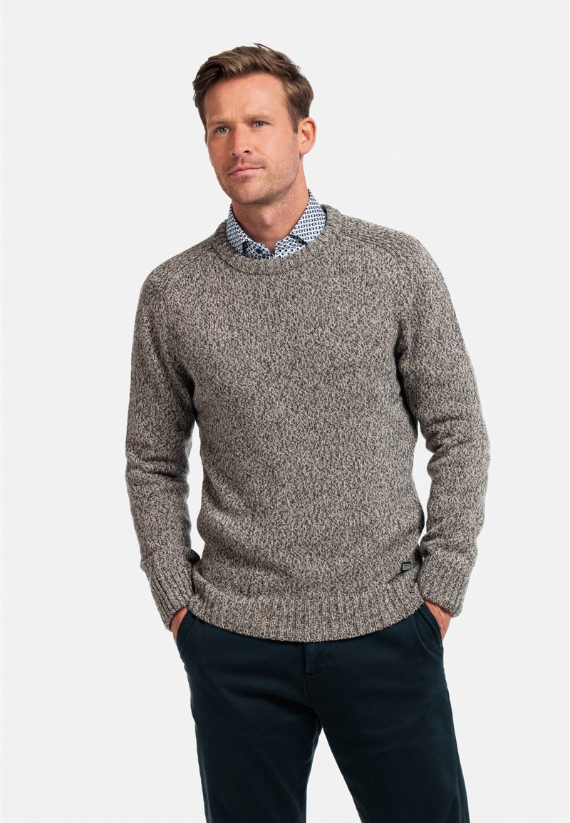 Grijze en beige gebreide trui met een ronde hals, met ribgebreide manchetten en zoom. Draagt over een gemusterde blauwe overhemd, tegen een neutrale achtergrond.