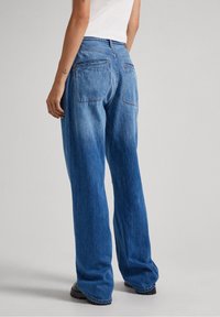 Blue denim wide-leg jeans with a faded finish, featuring two back pockets and a high-waisted design. Textured fabric detail visible.