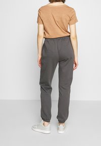 Brun kortärmad t-shirt i kombination med grå joggers, med en avslappnad passform, elastiska muddar och en slät yta. Vita sneakers fulländar looken.