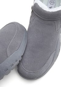 Pelēki zamšādas potīšu zābaki ar mīkstu, baltu flīsa oderi, zemu profilu dizainu un gumijas zoli ar teksturētu saķeri. Izmēra 37 birka redzama.