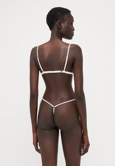 Set di lingerie in pizzo bianco con spalline regolabili, dotato di chiusura sul retro e design con perizoma sottile. Accenti hardware minimalisti arricchiscono il look.