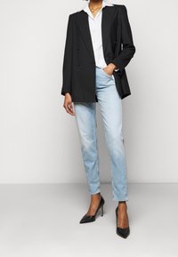 Svart dubbelknäppt kavaj med slag, vit skjorta, ljusblå jeans och svarta spetsiga stilettklackar.