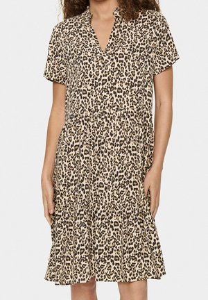 Kvinde iført en kjole med korte ærmer, der går til knæet, med et beige og sort leopardmønster og V-udskæring.