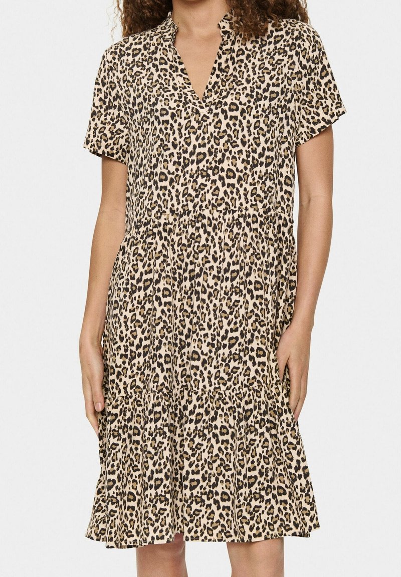 Femme portant une robe à manches courtes, longueur genoux, avec un motif léopard beige et noir et un col en V.