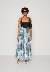 Jupe maxi avec des motifs bleu et vert vifs, associée à un haut noir ajusté. Comprend un détail de boutons, portée avec des chaussures blanches et un sac noir.