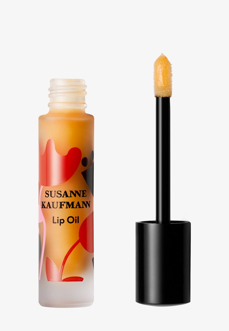 Frosted glass lip oil bottle with colorful abstract design labeled Susanne Kaufmann and black applicator with doe-foot tip dipped in peach lip oil.