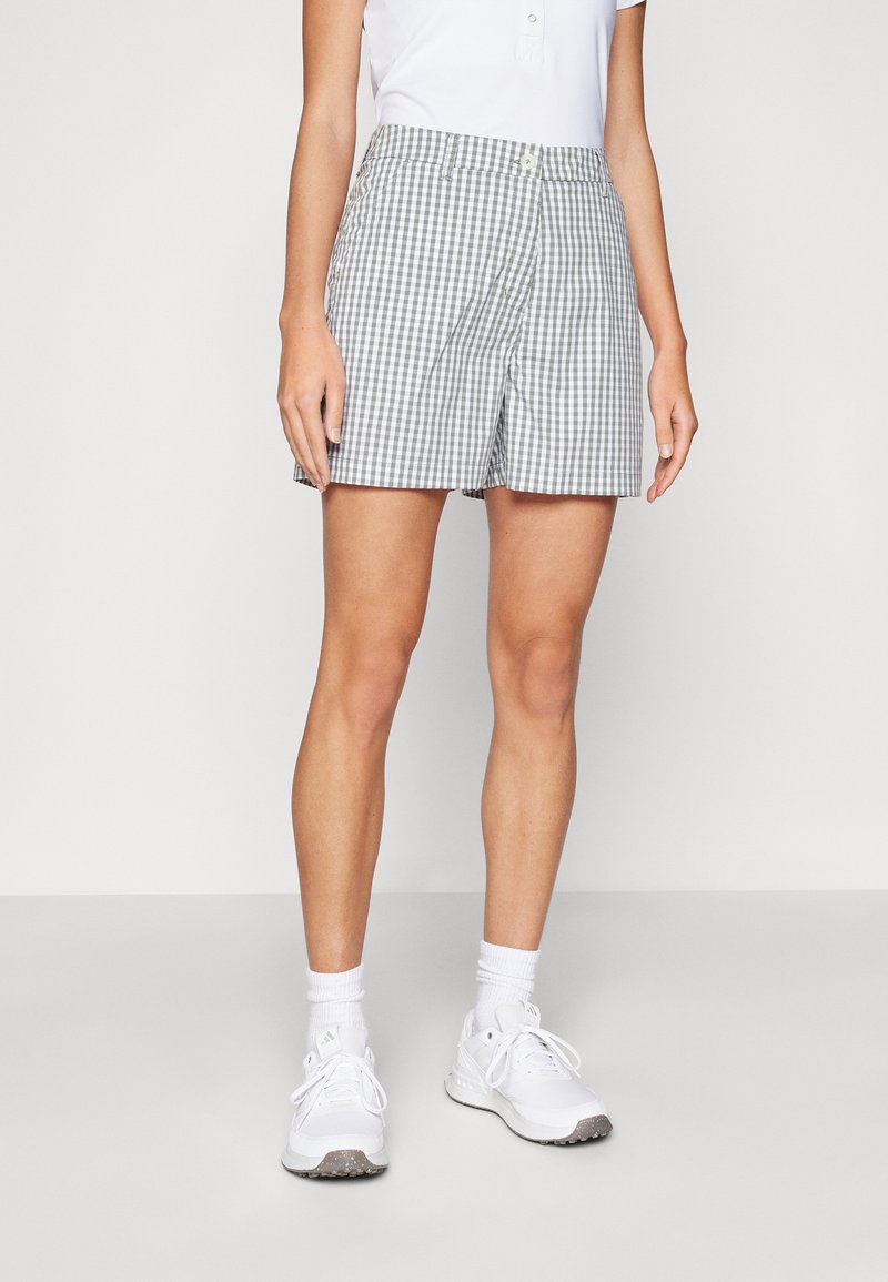 Pantalones cortos de cuadros grises y blancos con frente plano, cierre de botón y bolsillos laterales, combinados con zapatillas blancas y calcetines tobilleros.