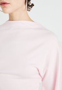 Lys rosa topp med en glatt tekstur og en tettsittende design, med høyt halslinje og lange ermer.