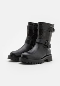 Bottines noires avec une finition en cuir lisse, des côtés texturés à motif serpent noir et deux sangles à boucle. Semelles en caoutchouc épaisses.