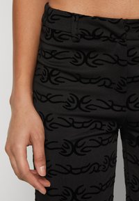 Zwarte broek met een gestructureerd patroon van gebogen lijnen in een donkerdere tint. De stof heeft een zachte, gladde afwerking met een aansluitend ontwerp.