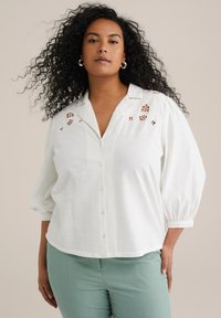Camicia bianca con bottoni, dal taglio rilassato, con ricami floreali sulle spalle e maniche a tre quarti.