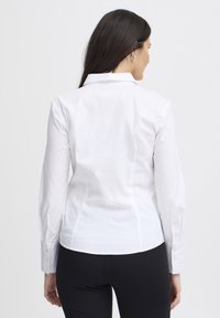 Camicia bianca a maniche lunghe con colletto classico, caratterizzata da una texture liscia e un design aderente. Cuciture sartoriali sul retro.