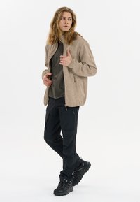 Beige zip-up fleecejacka över en mörkgrön skjorta, tillsammans med svarta cargobyxor och svarta vandringskängor med bra grepp.