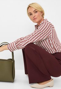 Blusa a righe rossa e bianca, pantaloni larghi bordeaux, ballerine beige chiare a punta e una borsa verde oliva con dettagli a zip.