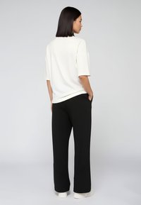 Witte oversized t-shirt met korte mouwen, gecombineerd met zwarte wijde broek en witte sneakers, gezien van achteren.