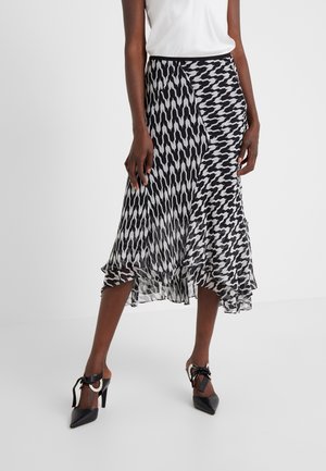 Femme portant une jupe midi asymétrique à motif noir et blanc, associée à des escarpins noirs pointus avec des brides à la cheville.