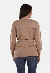 Cardigan a maglia marrone chiaro con texture a coste su spalle e maniche. Presenta una vita con cintura e un dettaglio di bottone sul collo.