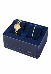 Goldfarbene Uhr mit Kettengliederarmband und goldfarbener Armbanduhr, präsentiert in einer navy-blauen Box mit samtiger Innenauskleidung und goldener Schrift.