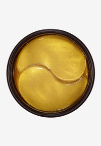 Patches pour les yeux en gel doré dans un conteneur noir rond. Les patches ont une texture lisse et scintillante et une forme incurvée de yin-yang.