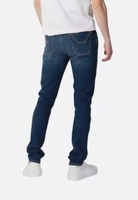 Jeans in denim blu scuro con una vestibilità slim, caratterizzati da un classico design a cinque tasche e cuciture in evidenza sulle tasche posteriori. Indossati con sneakers bianche.