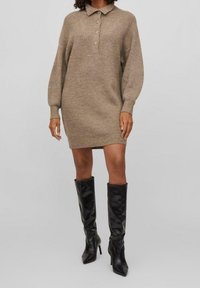 Koftklänning i beige med krage, placket med fyra knappar och puffärm, matchad med höga svarta läderstövlar.