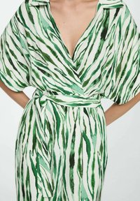 Groen en wit gestreepte wikkeljurk met een V-hals, korte mouwen en een gestrikte tailleband. De stof lijkt lichtgewicht met een gladde textuur.