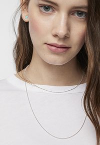 Collar de cadena de plata con dos hilos, que presenta un delicado diseño de cuentas. La modelo lleva pendientes de botón pequeños en turquesa.