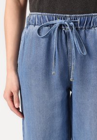 Svetlo modri jeans hlače z elastičnim pasom in nastavljivim vrvico. Imajo stranske šive in sproščen kroj.