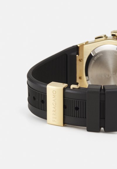 Black silicone watch strap with a textured surface, featuring a gold metal clasp engraved with “FERRAGAMO” and a metal case.