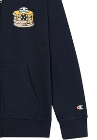Granatowy hoodie na zamek wykonany z miękkiego materiału, z graficznym wzorem naleśnika na lewej piersi oraz małym logo na mankiecie prawego rękawa.