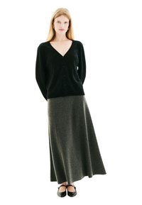 Gilet noir en maille avec un col en V et un motif en diamant, associé à une longue jupe grise en matière douce, agrémenté de ballerines noires.