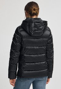 Czarna pikowana kurtka puchowa z kapturem, z przeszyciami i elastycznymi mankietami. Tkanina ma połyskującą, gładką fakturę.