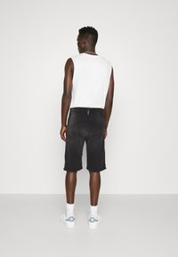 Pantaloni scurți din denim negru cu croială dreaptă, având buzunare la spate și detalii cu cusături vizibile. Purtați cu un top alb fără mâneci și adidași.