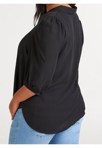 Černý pulovrový top s kulatým lemem, krátkými nabíranými rukávy a límcem. Nosený s světle modrými džíny, které ukazují hladkou texturu látky.