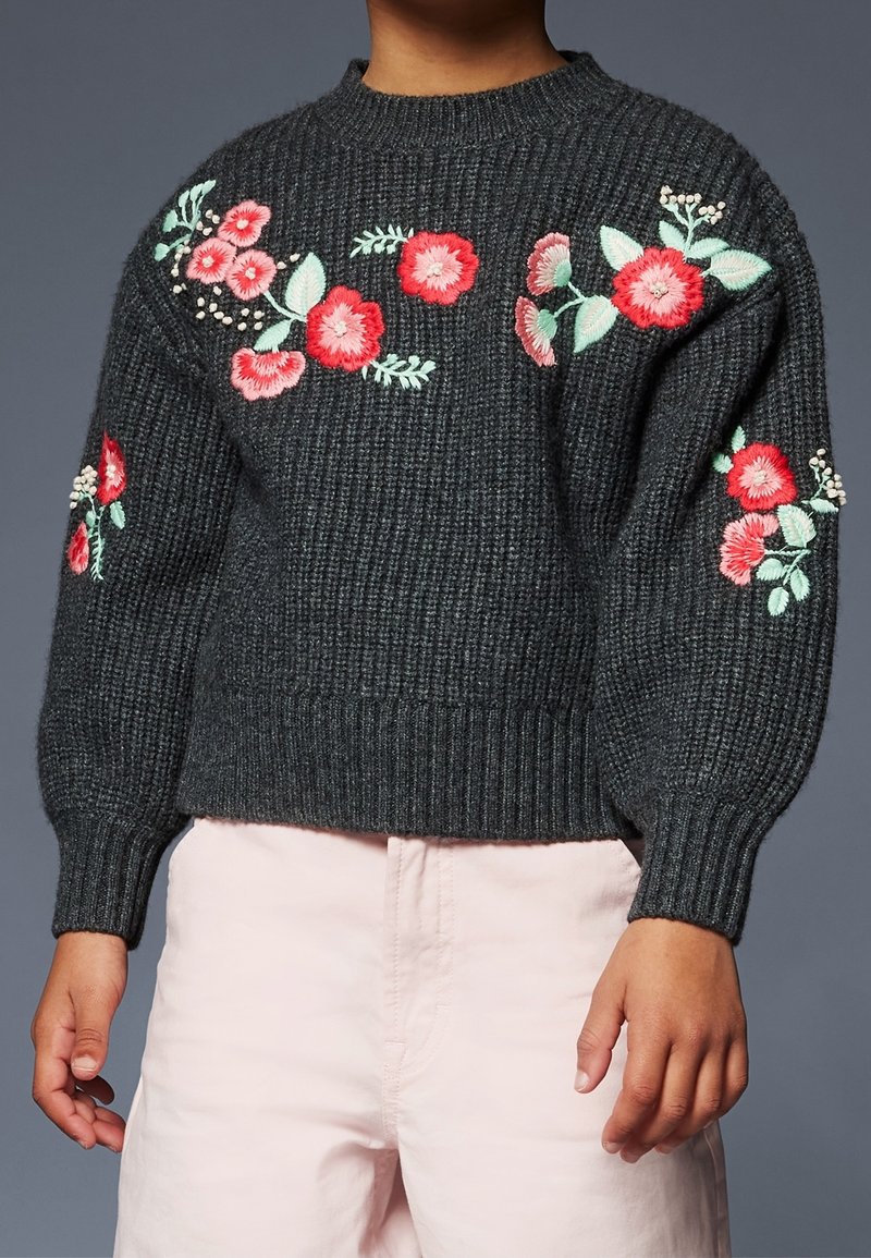 Pull en maille gris foncé avec texture côtelée, orné de broderies florales colorées sur les manches et le devant. Manches longues, col ras du cou.